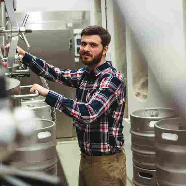 A man in plaid shirt working with beer kegs.