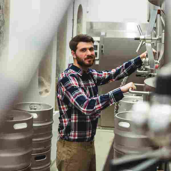 A man working in a brewery with many kegs.